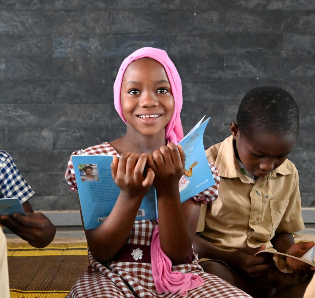 A smiling girl holding a blue book in class