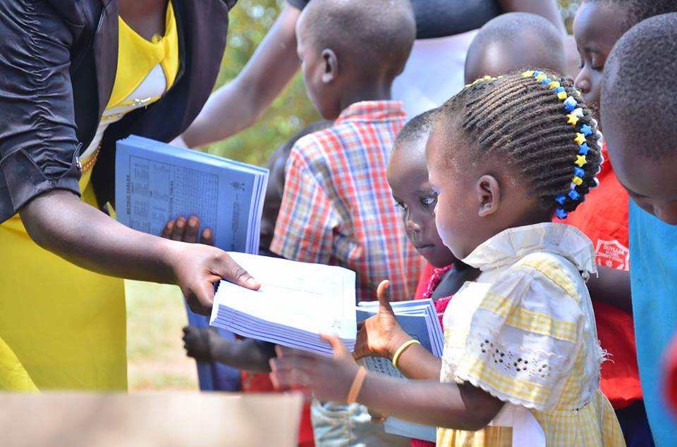 A volunteer handing books to young children outdoors