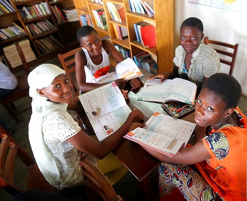 Learners gathered around textbooks in a library setting